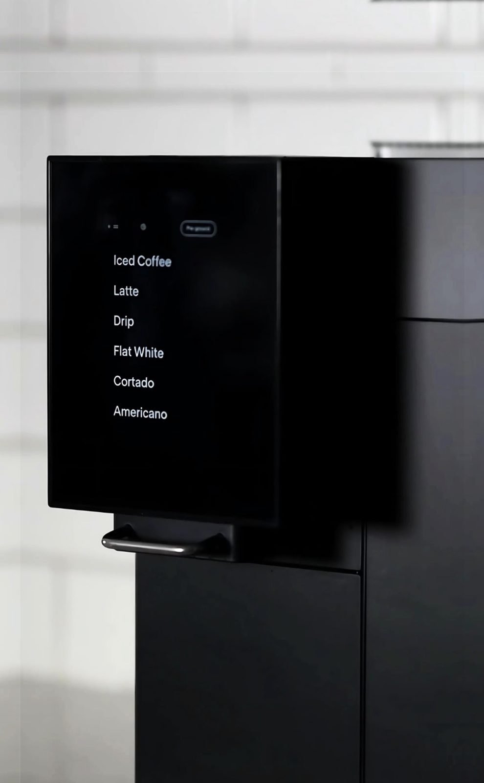 A matte black coffee machine with its drink menu lit up: iced coffee, latte, drip, flat white, cortado, Americano