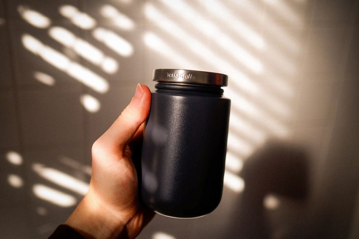 A hand holding a navy Terra Kaffe canister in slatted window light