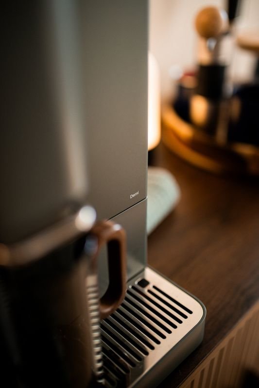 The Demi wordmark above the drip tray, a mug in soft focus in front