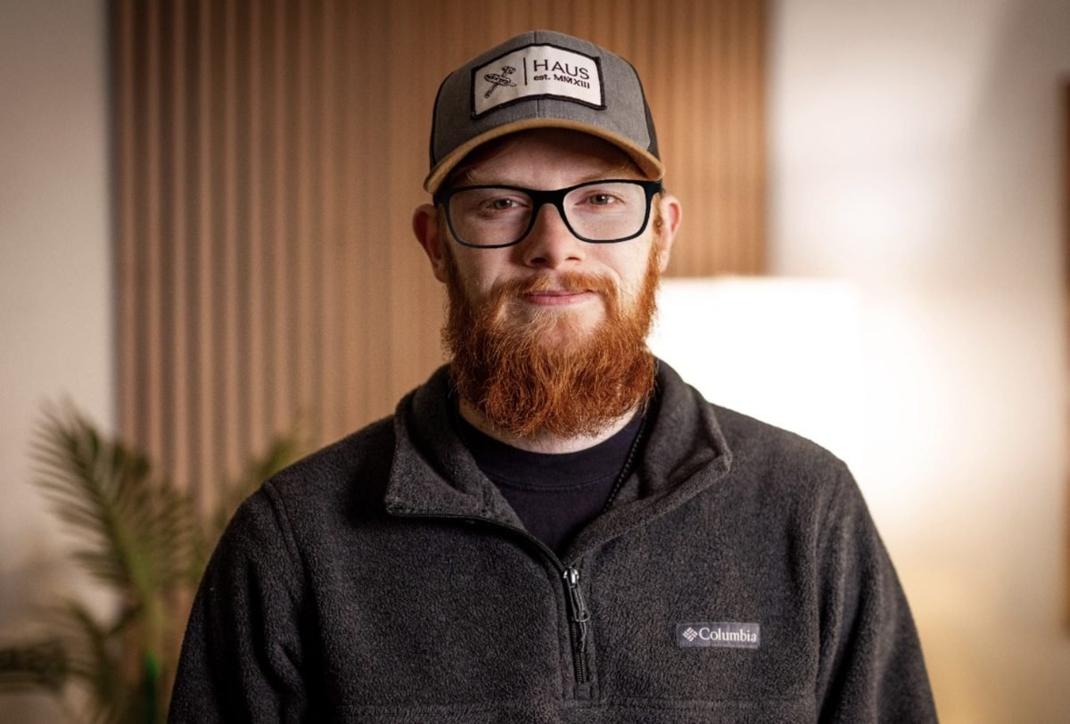 A bearded man in a cap and fleece, smiling in warm light