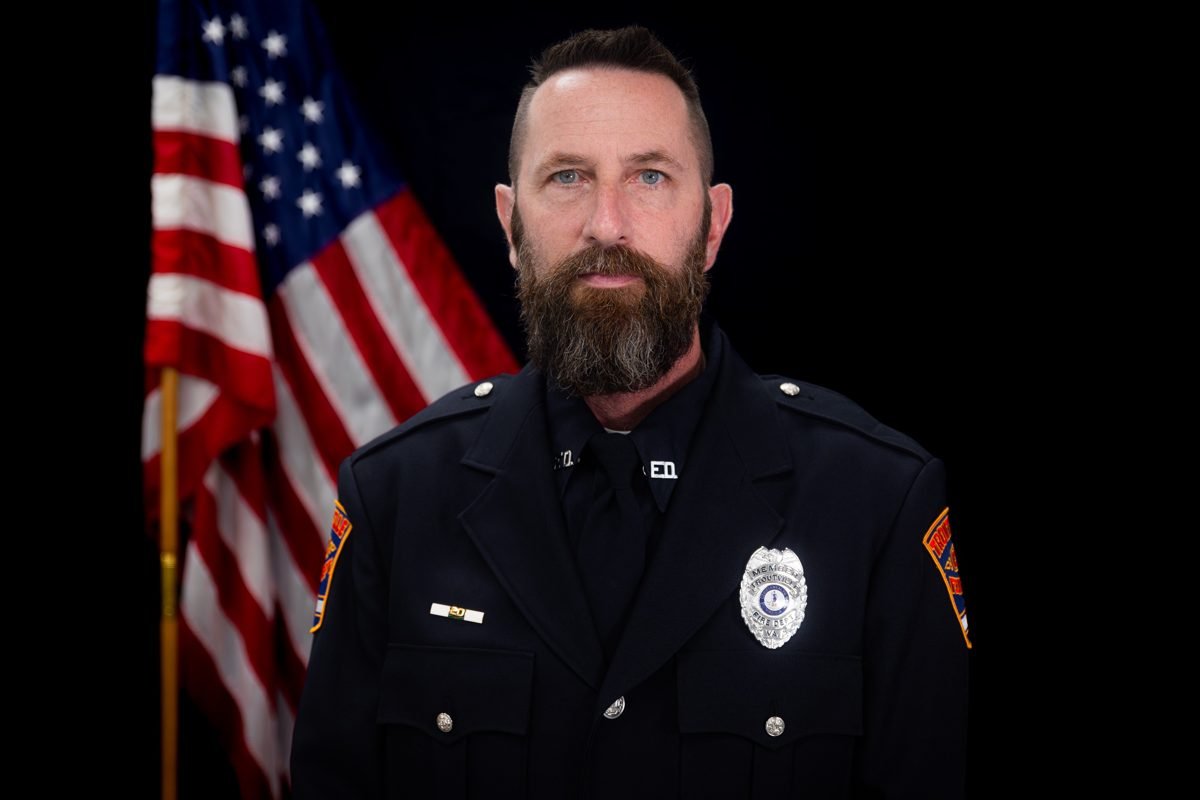 A bearded firefighter in dress uniform in front of an American flag