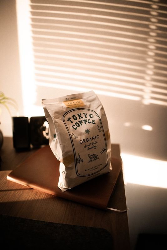 The Tokyo Coffee bag standing on a leather notebook, blinds casting stripes on the wall behind
